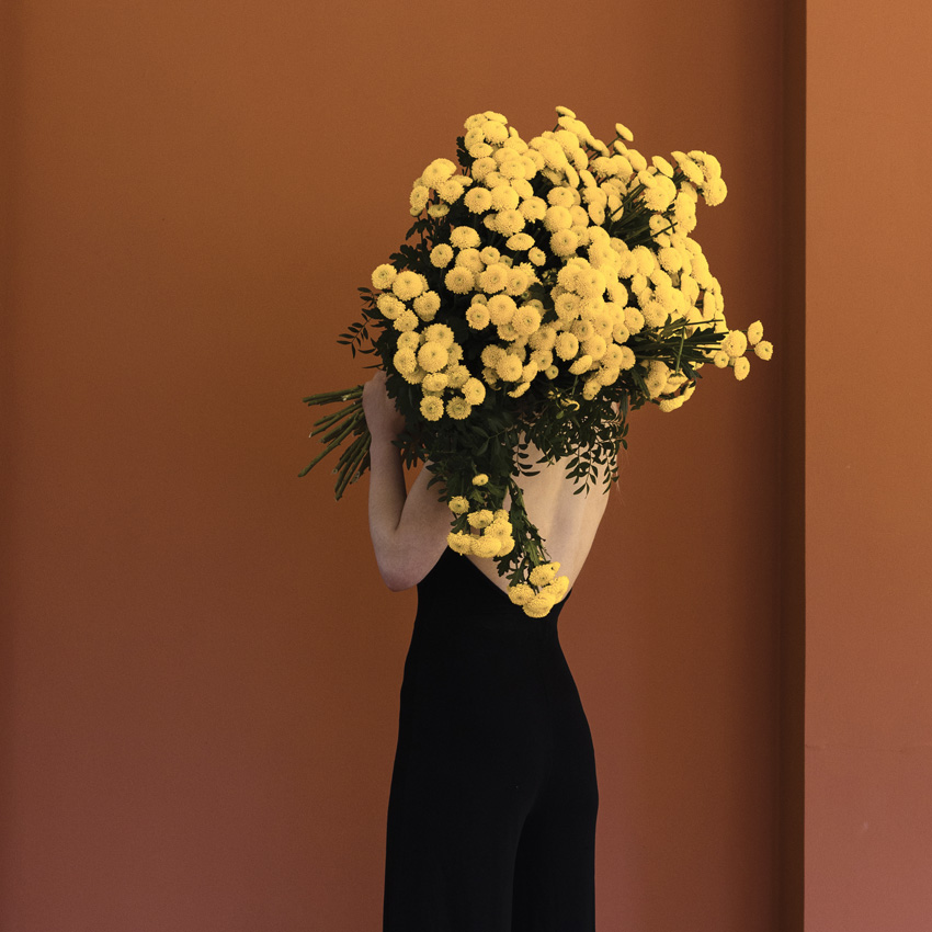 Woman in black with her back turned to the camera and holding a bouquet of yellow chrysanthemum