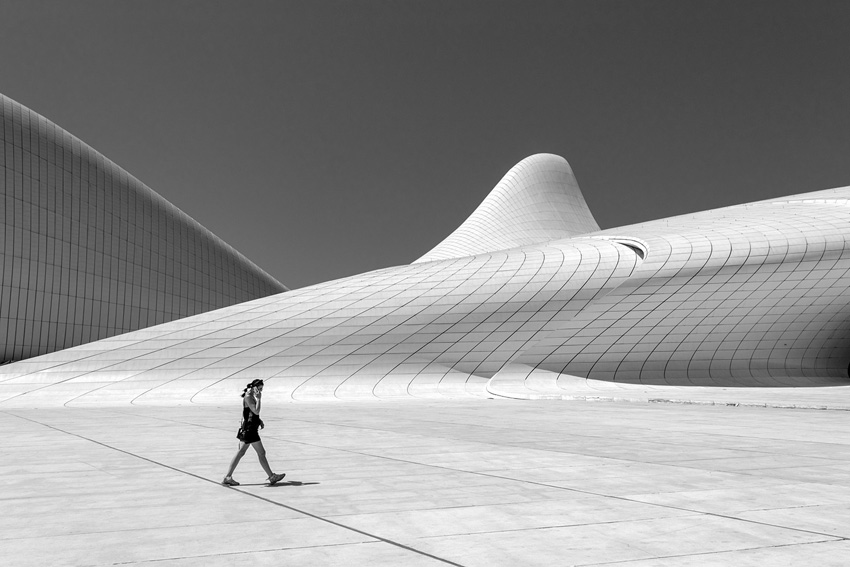 Lone figure on the phone walking in front of a curved building